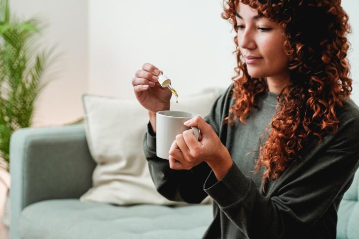 person putting tincture dropper in mug